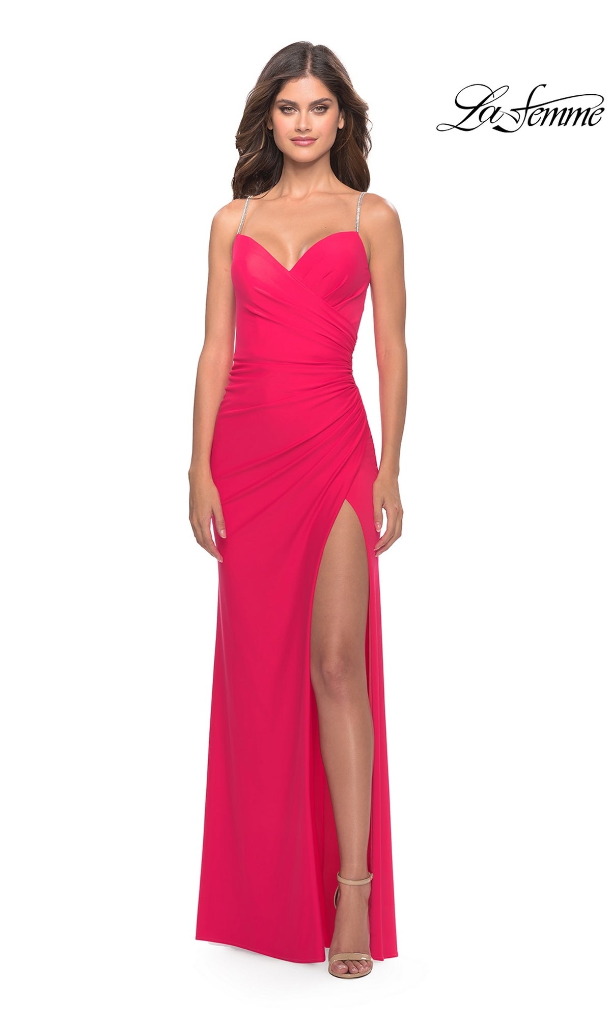 A woman wears the La Femme Hot Coral Pink Prom Dress 31224 with spaghetti straps, a sweetheart neckline, and a thigh-high slit, standing against a white background.